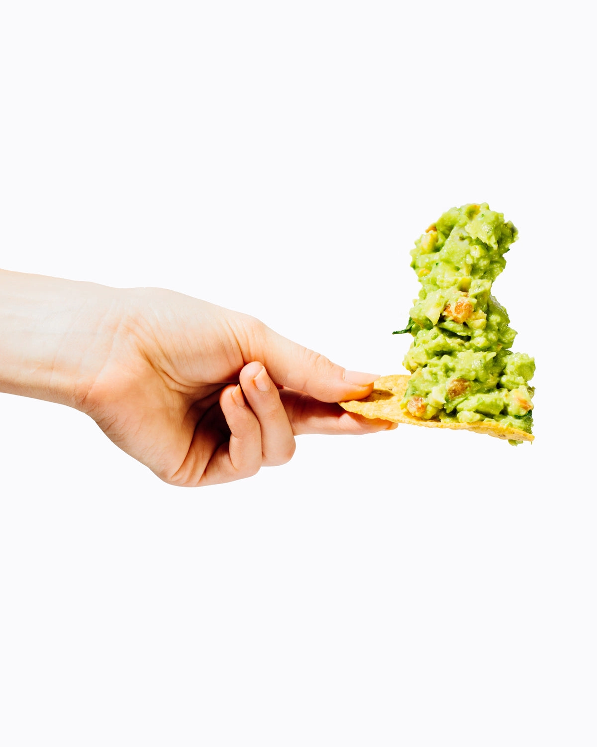 A hand holding a tortilla chip loaded with guacamole